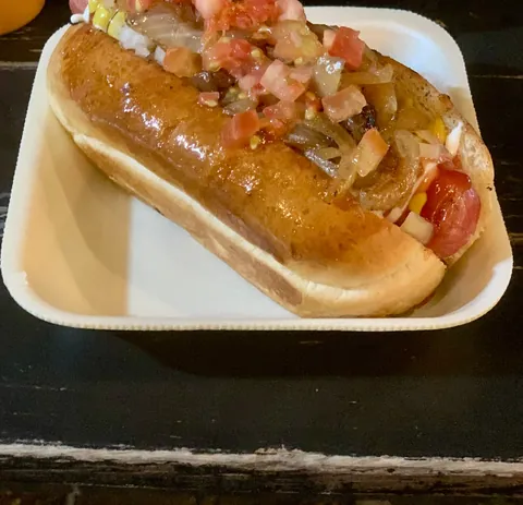 Hotdog con cebolla asada y tomate picado en pan dorado